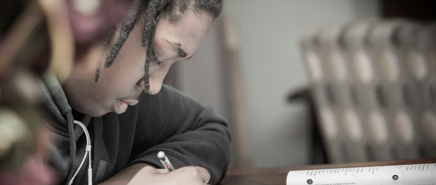 man writing on paper near book on table