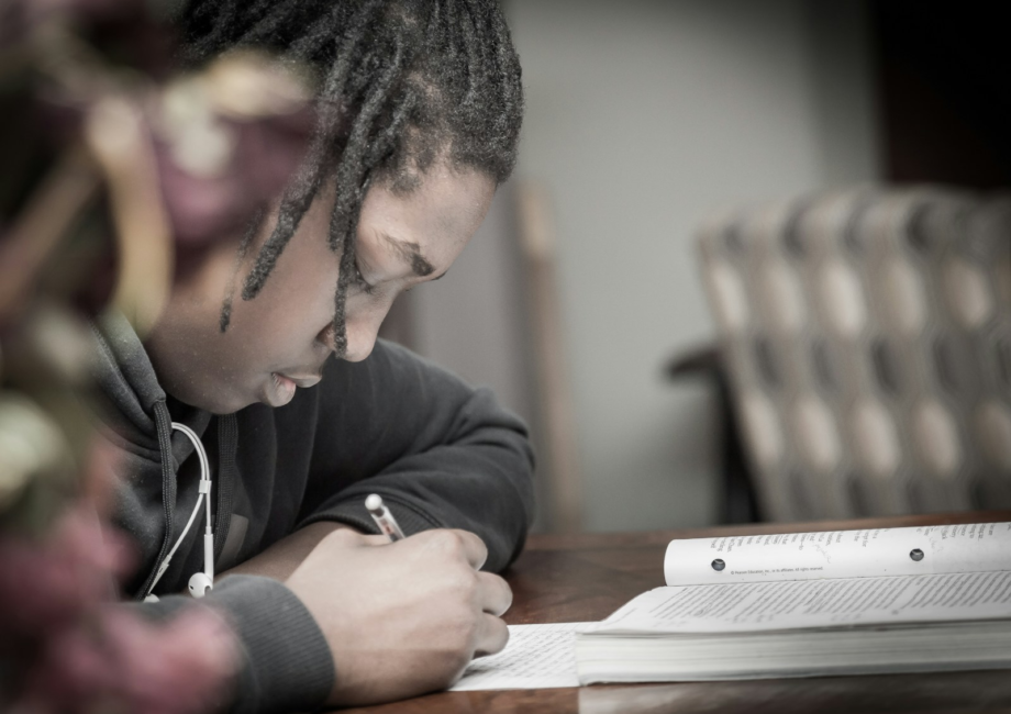 man writing on paper near book on table