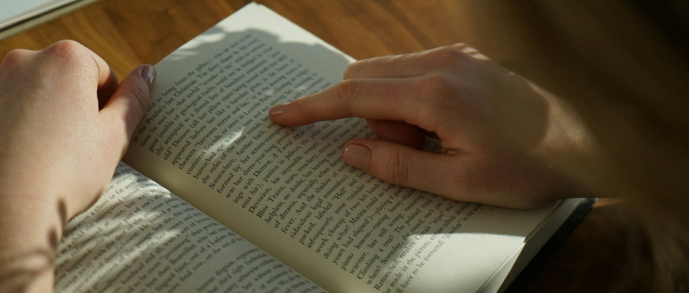 person reading book on brown wooden table taken at daytome