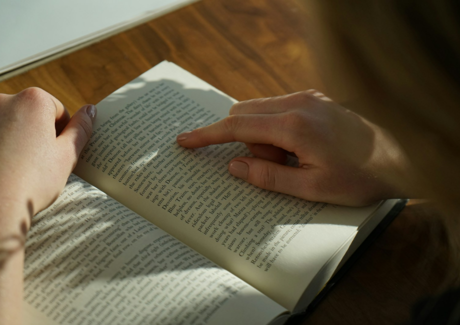 person reading book on brown wooden table taken at daytome